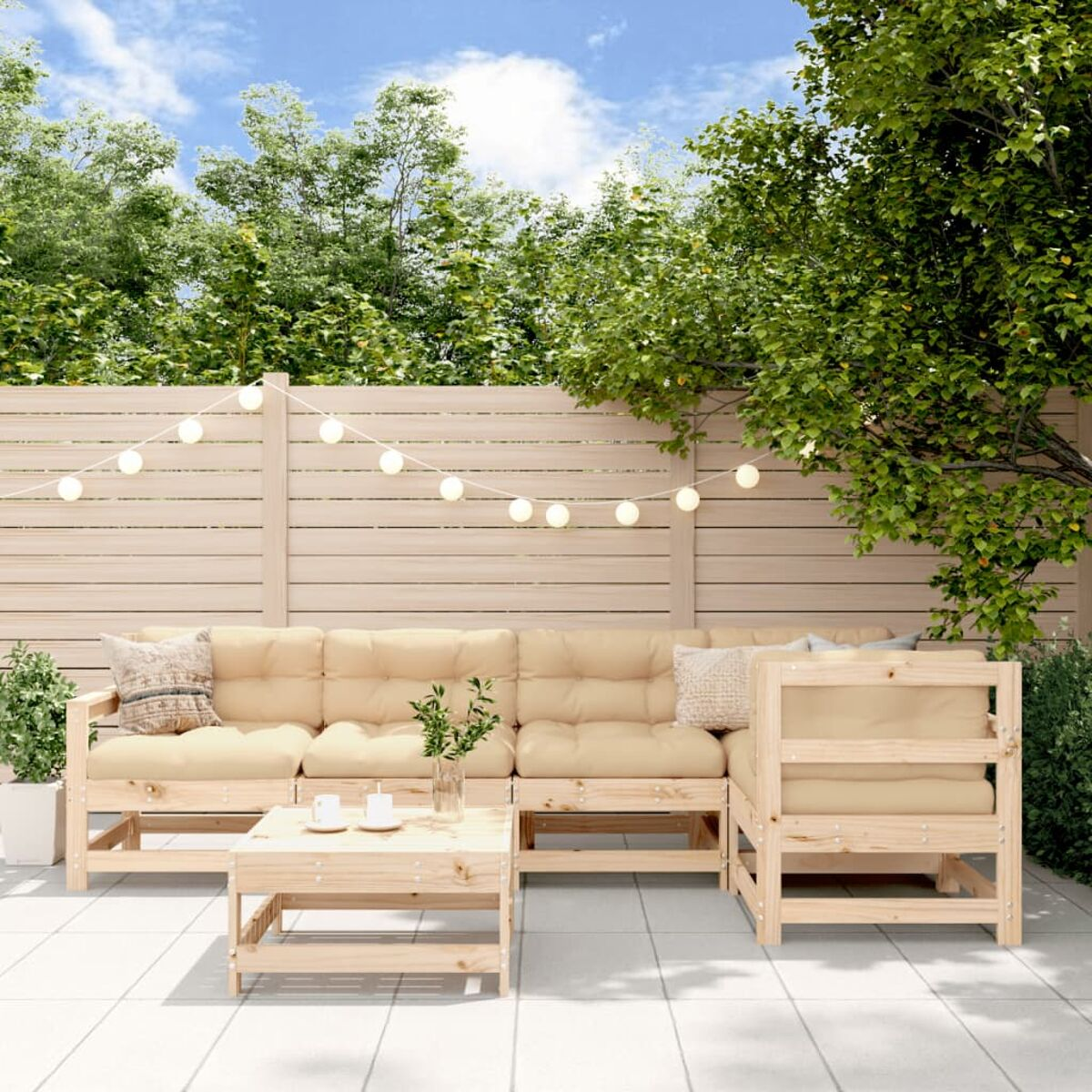 Terrassenszene im Freien mit hellen Holzmöbeln, Kissen und Dekorationen, sonnigem Himmel im Hintergrund.
