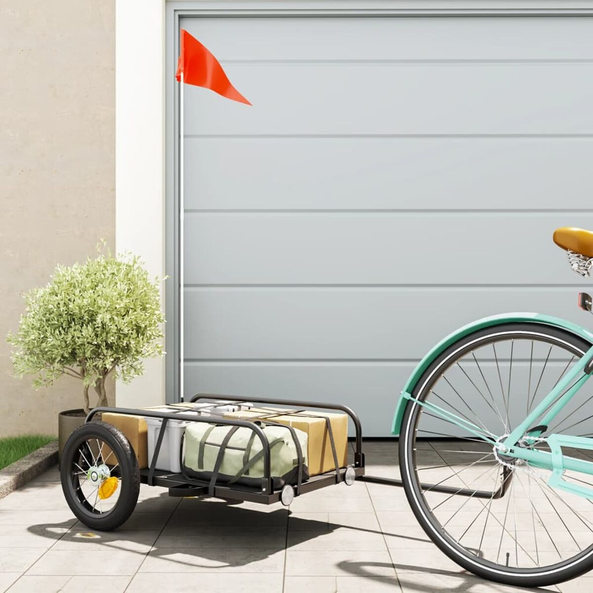Fahrrad mit Anhänger, beladen mit Paketen, rote Fahne am Anhänger, in der Nähe einer Garage.