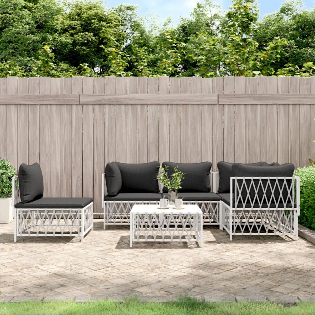 Gartenset mit weißem Rahmen und schwarzen Kissen, kleinem Tisch und Holzzaun im Hintergrund.