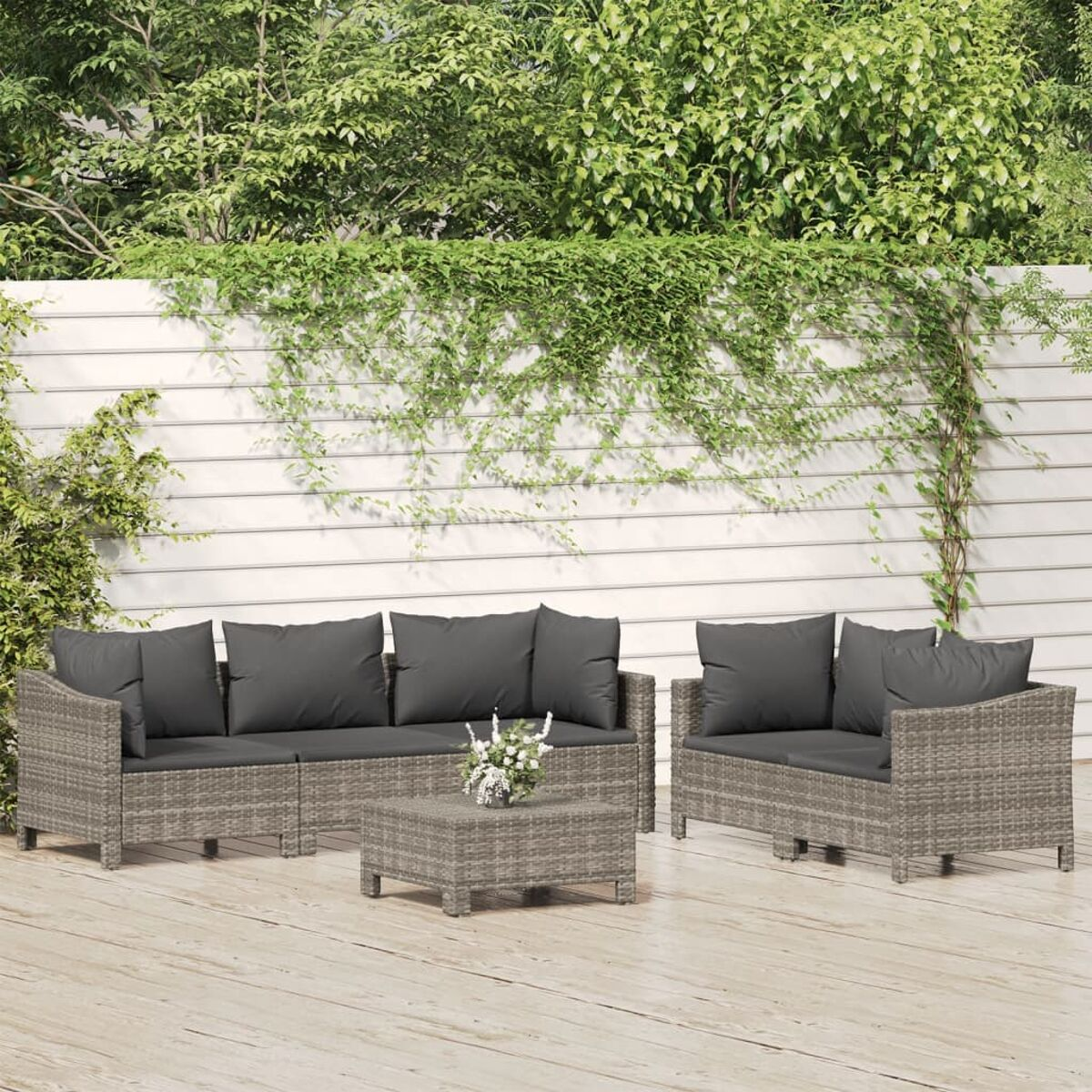 Outdoor-Sitzgruppe mit grauen Kissen, grauem Korbrahmen und Couchtisch. Holzterrasse und Efeu.