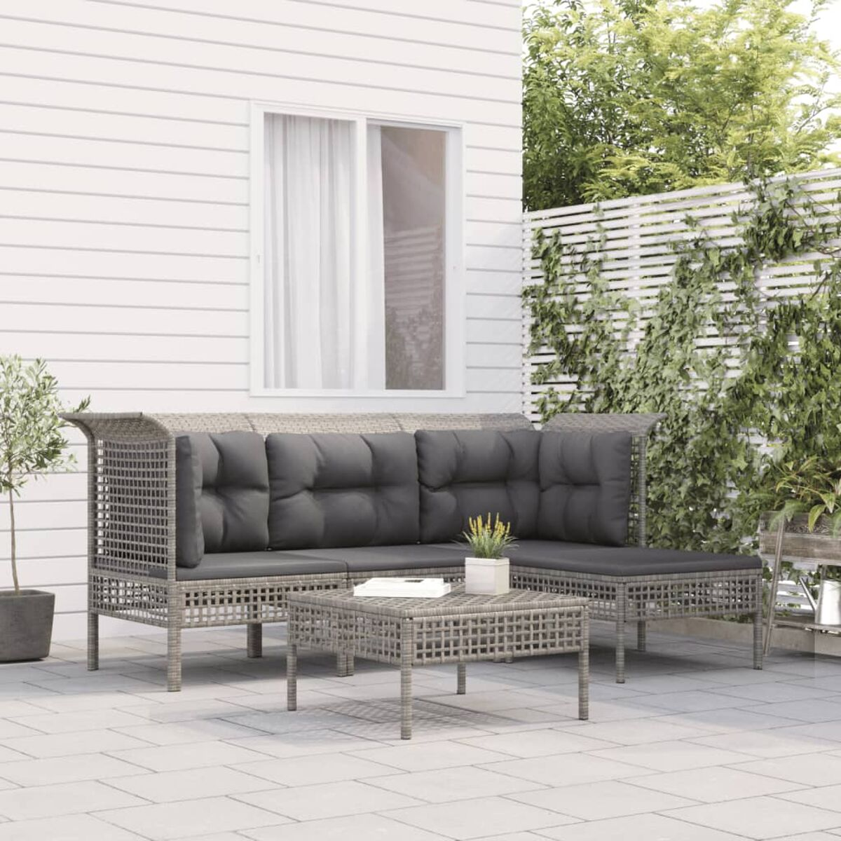 Terrassenset im Freien mit Sofa, Couchtisch und Pflanzen. Weiße Verkleidung und Zaun im Hintergrund.