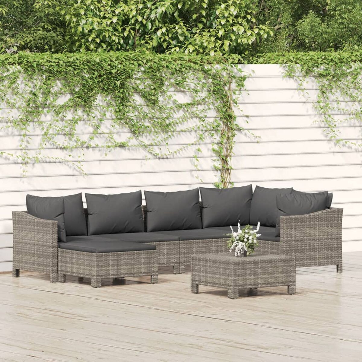 Outdoor-Sitzgruppe mit grauen Kissen, quadratischem Tisch und weißem Zaun im Hintergrund.