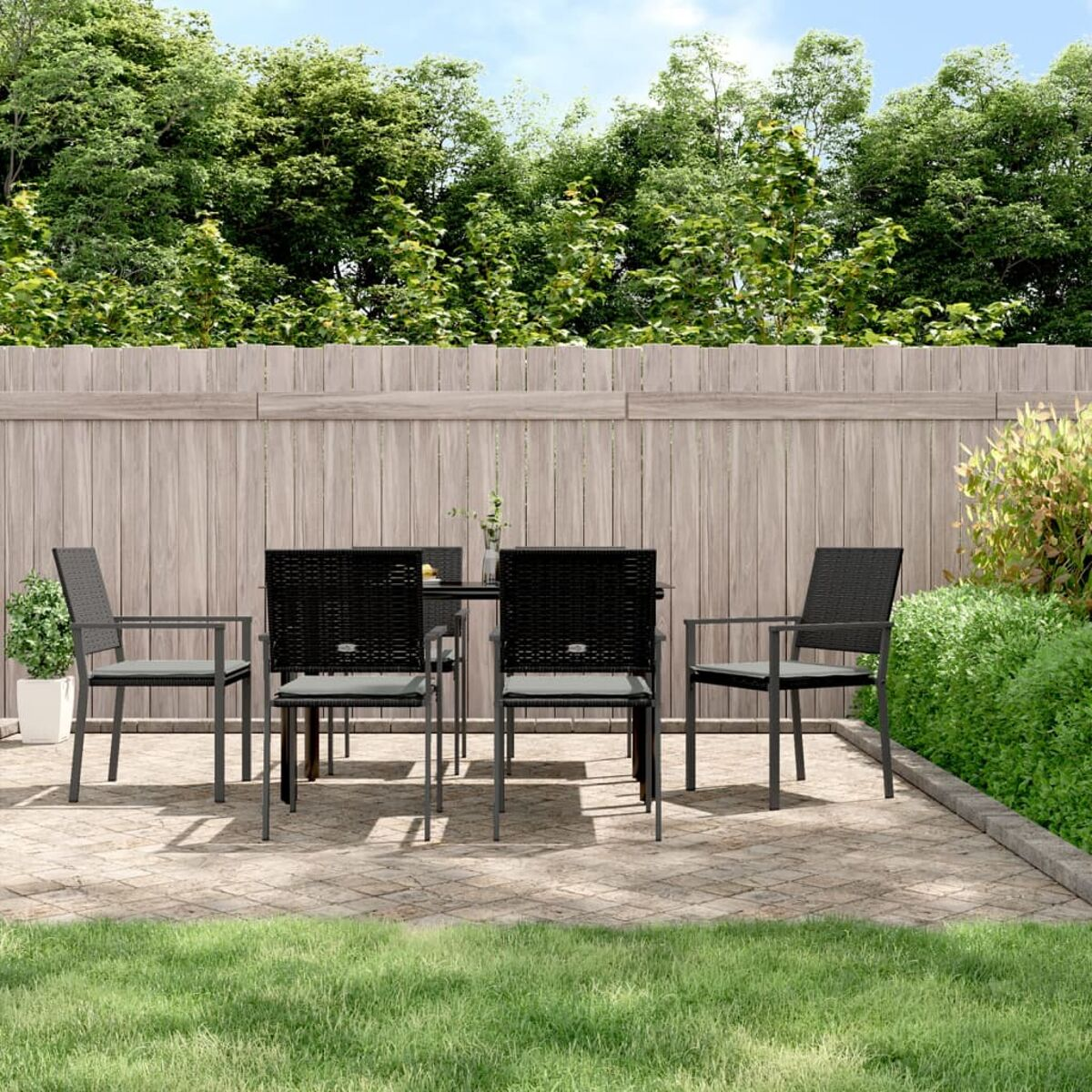 Terrassenset im Freien mit Tisch und Stühlen auf Ziegel. Grünes Gras und Holzzaun im Hintergrund.