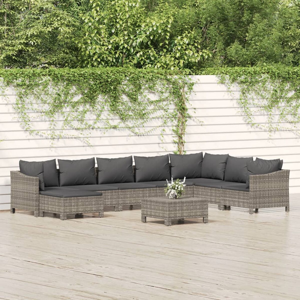 Outdoor-Ecksofa mit grauen Kissen, Couchtisch. Holzterrasse und Efeu. Sonniger Tag.