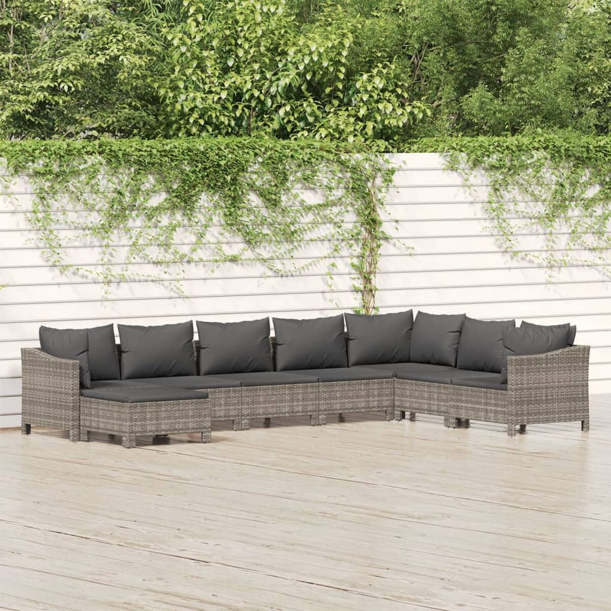 Ein Gartenmöbel-Set auf einer Terrasse. Es hat graue Kissen. Der Hintergrund ist eine Wand.
