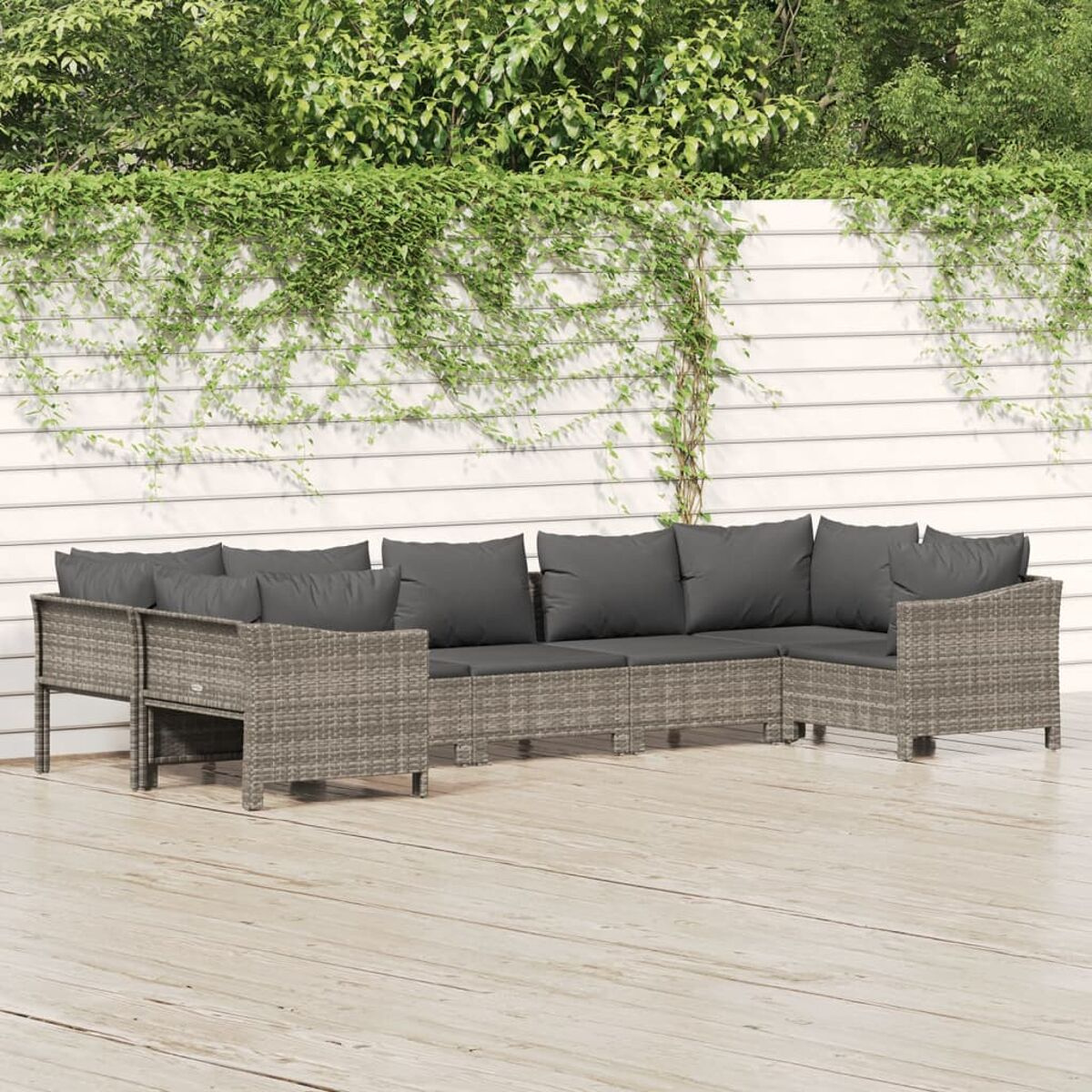 Ein graues Rattan-Sofaset auf einem Holzdeck, mit weißem Zaun und Grün im Hintergrund.