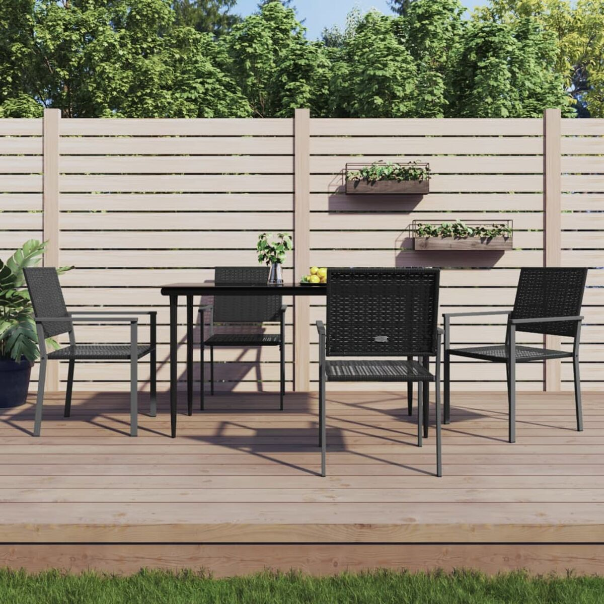 Ein schwarzes Ess-Set mit einem schwarzen Tisch und Stühlen auf einer Holzterrasse, mit Zaun und Bäumen.