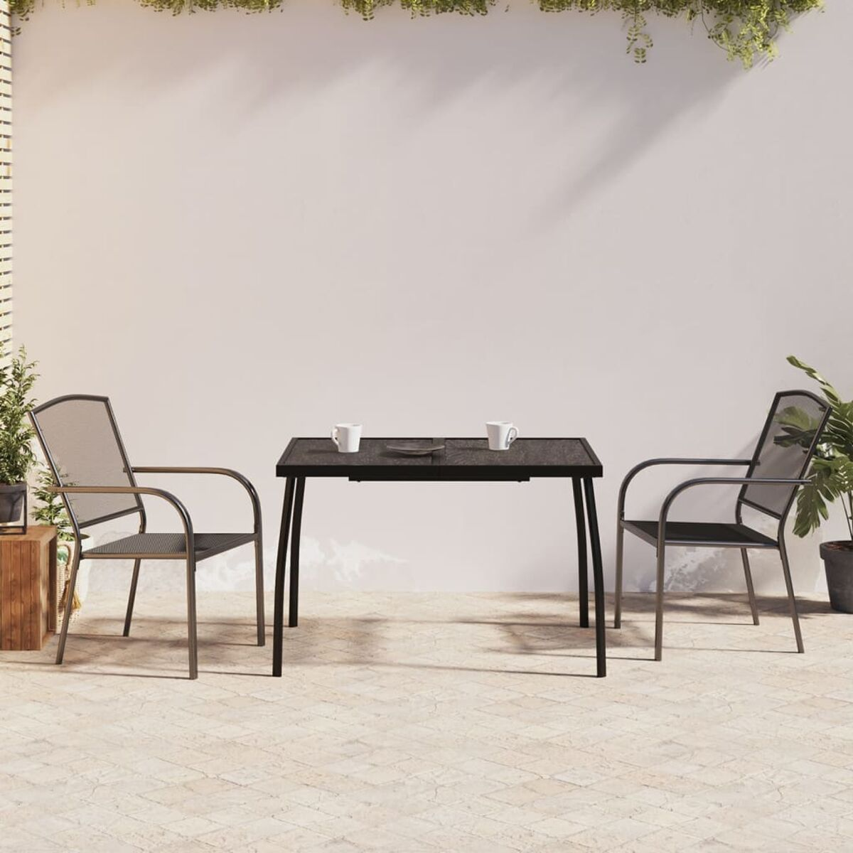 Terrassensitzgruppe im Freien mit schwarzem Tisch und zwei Stühlen. Weiße Wand und Pflanzen im Hintergrund.