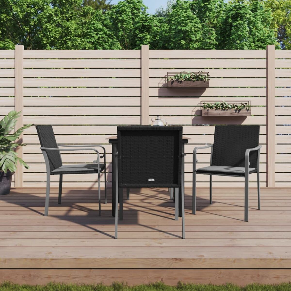 Essgruppe im Freien auf einem Holzdeck. Schwarze Stühle und Tisch mit silbernen Rahmen. Grünes Gras dahinter.
