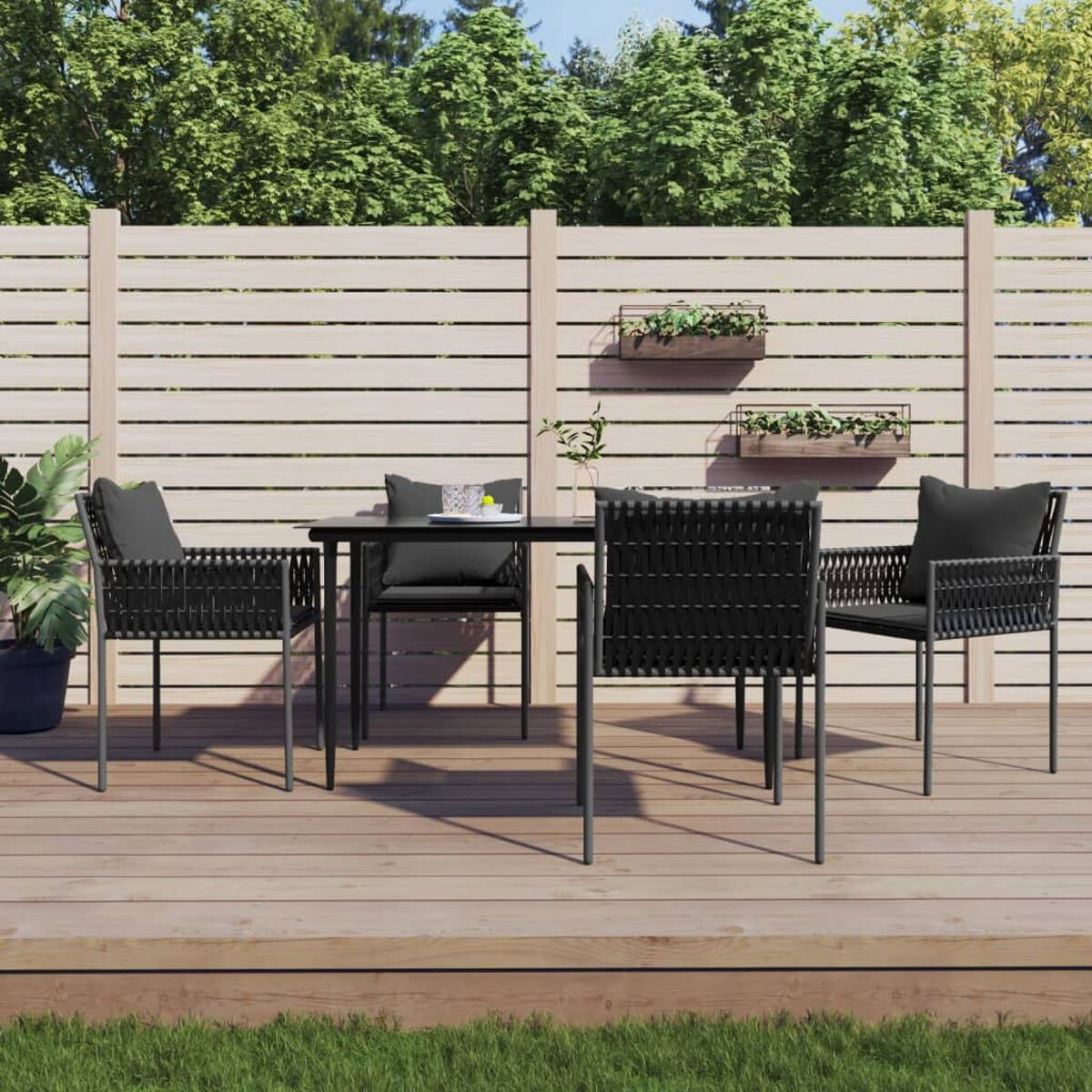 Ein Terrassenset auf einem Deck: Tisch, 4 Stühle, schwarze Kissen und Holzzaun im Hintergrund.