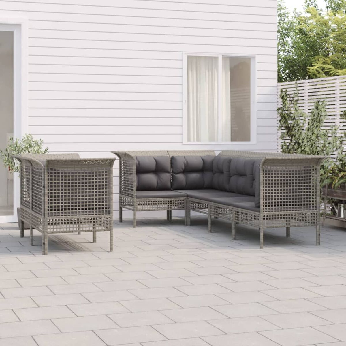 Outdoor-Ecksofa mit grauen Kissen. Weiße Verkleidung im Hintergrund.