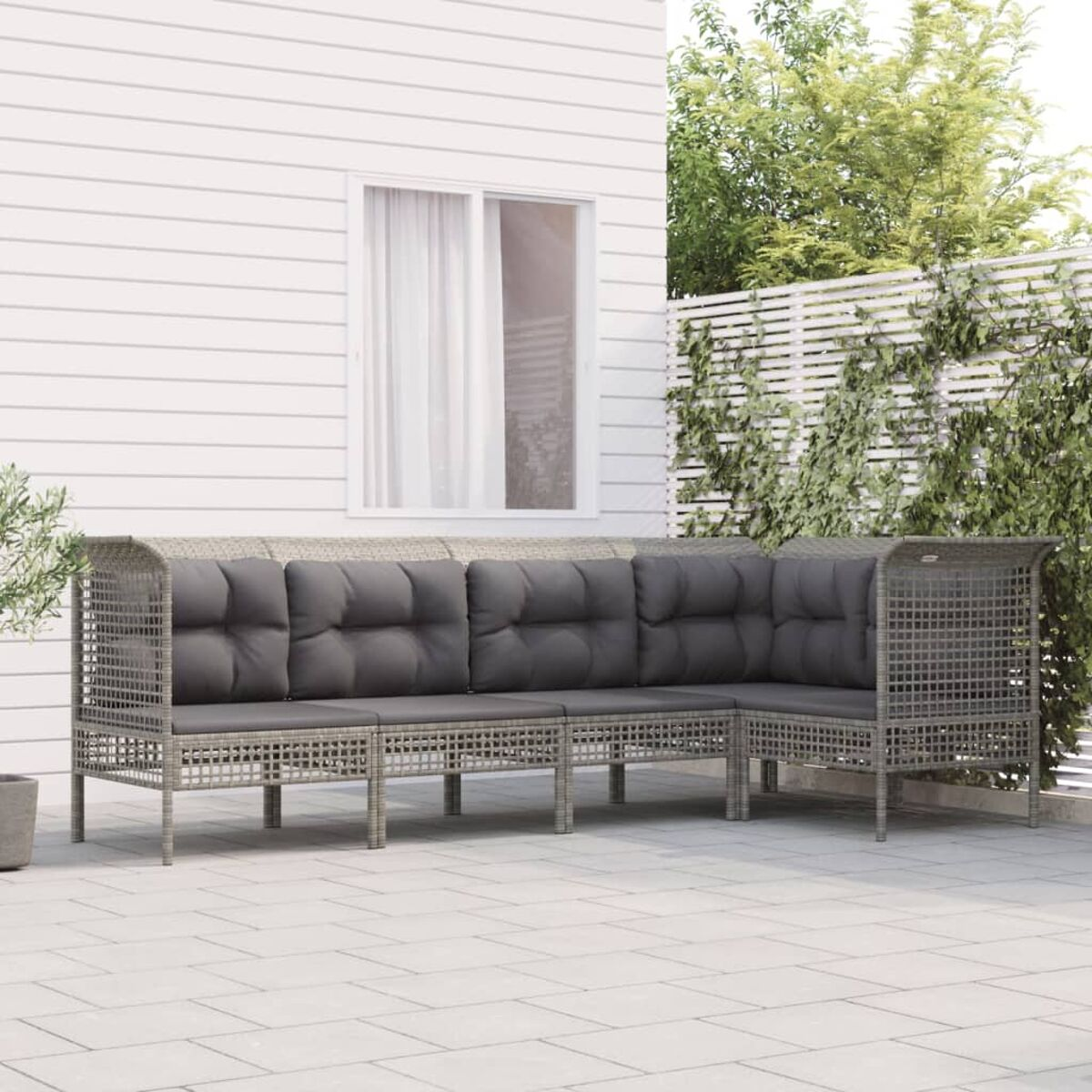 Graues L-förmiges Outdoor-Sofa mit grauen Kissen. Weiße Wand und grüne Pflanzen im Hintergrund.