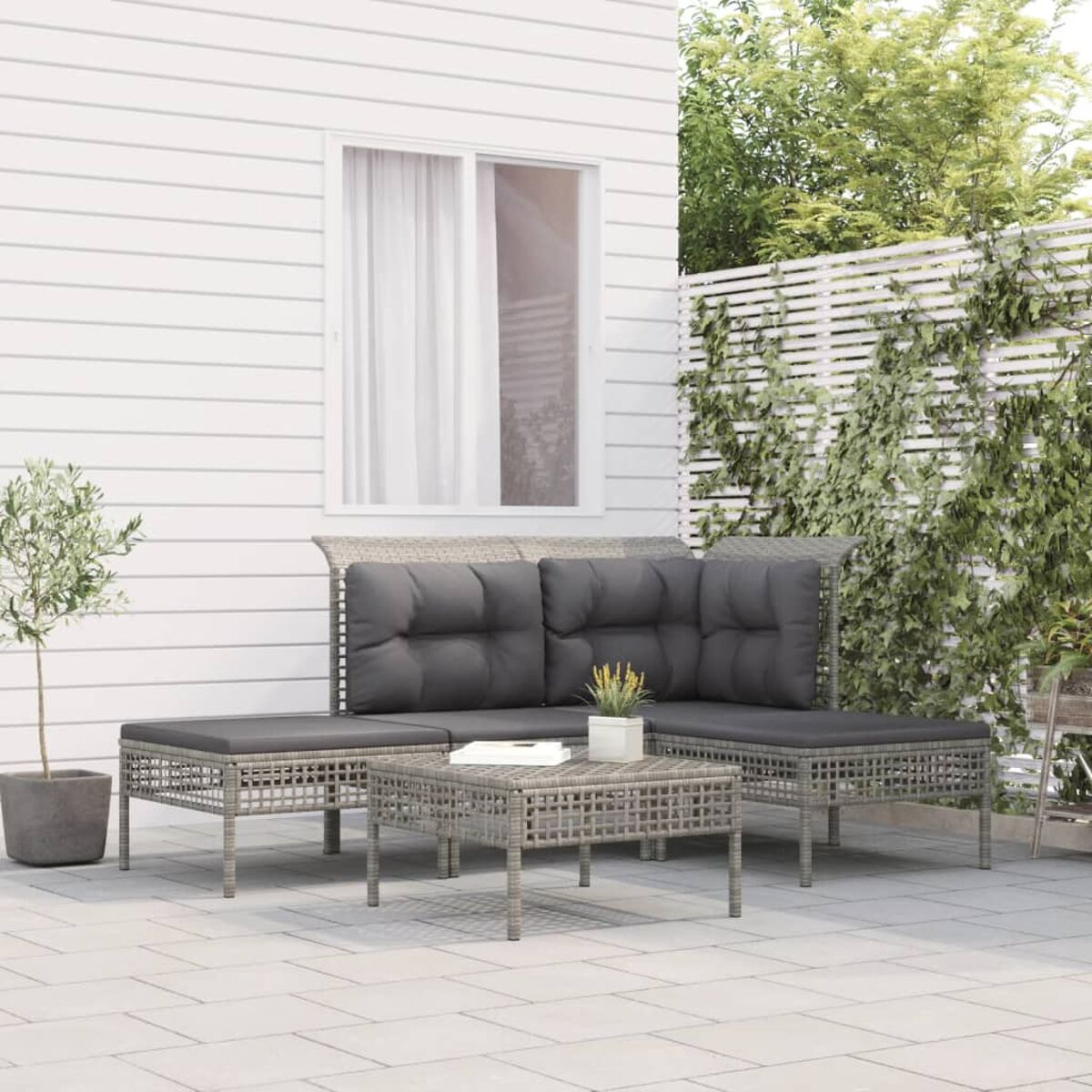 Sitzbereich im Freien mit grauen Kissen, Couchtisch und weißem Wandhintergrund.