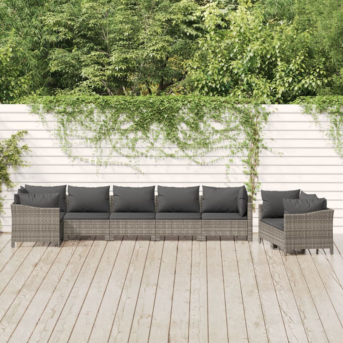 Gartenmöbel-Set. Graue Kissen, gewebtes Design. Holzterrasse. Grün im Hintergrund.