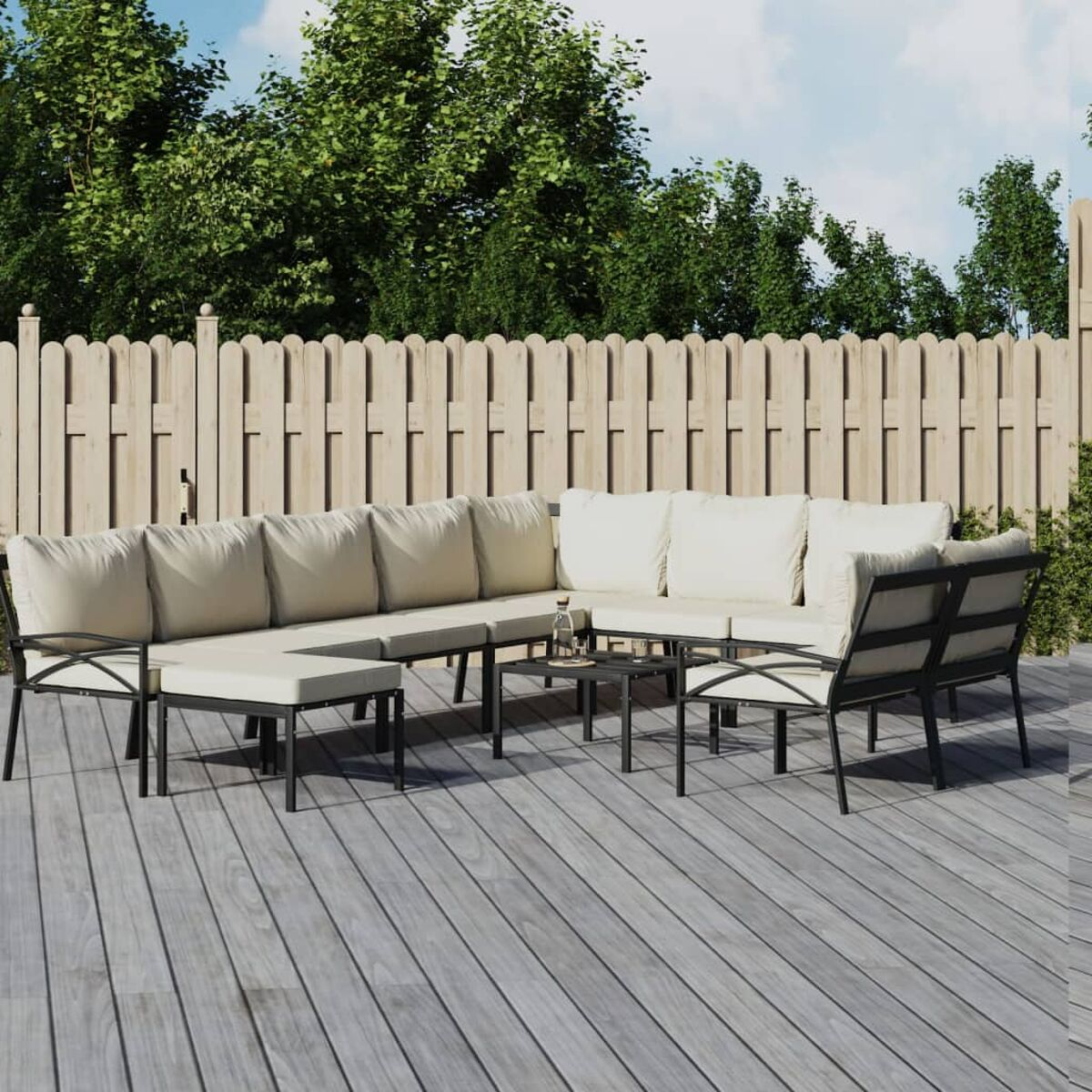 L-förmige Outdoor-Sofagarnitur mit cremefarbenen Kissen auf einem Holzdeck. Hintergrund: Holzzaun und Bäume.