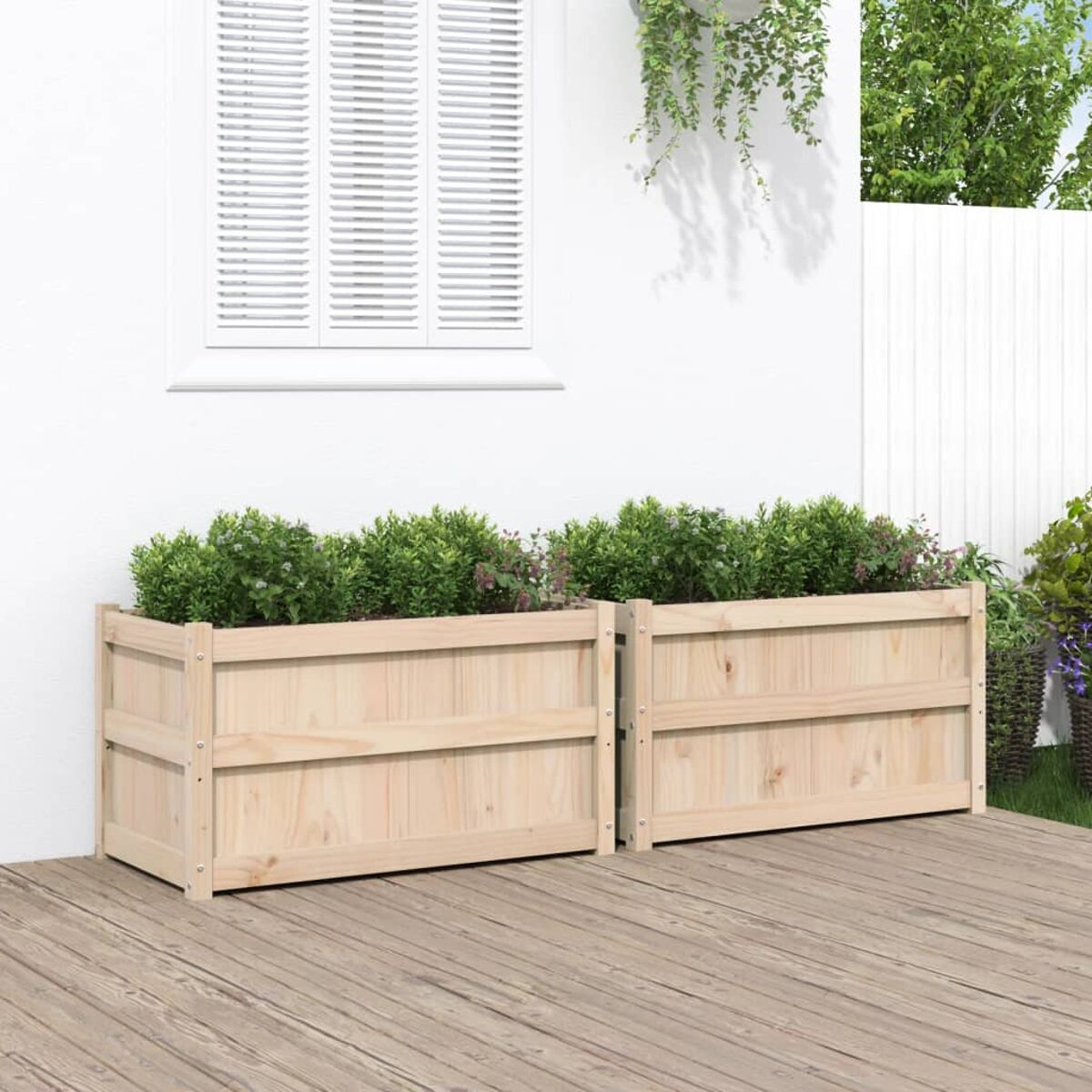 Zwei Holzpflanzkästen mit Pflanzen auf einer Holzterrasse vor einer weißen Wand.
