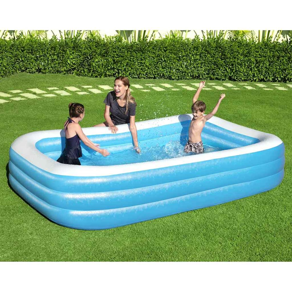 Kinder spielen in einem blauen aufblasbaren Pool in einem grasbewachsenen Garten.