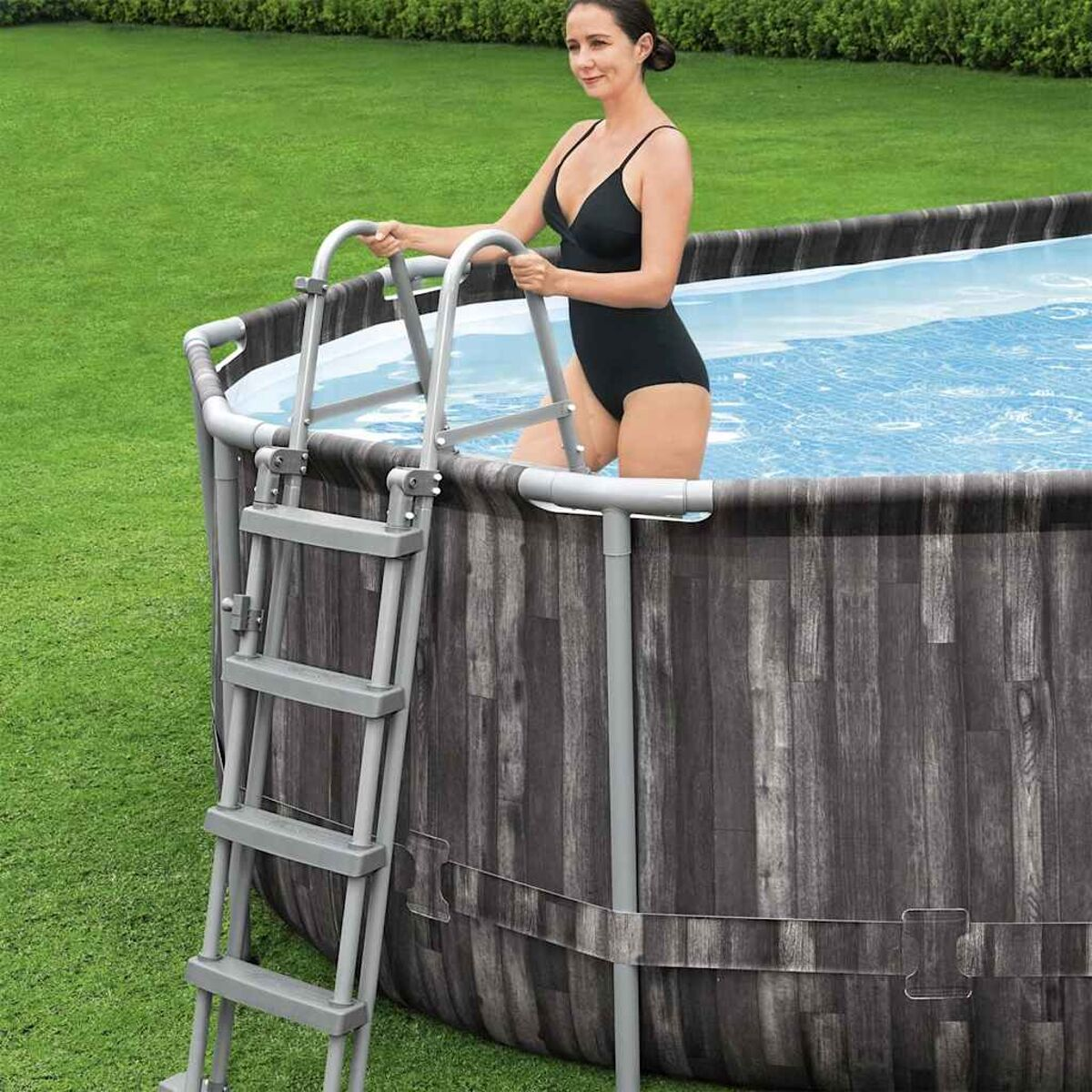 Eine Frau in einem schwarzen Badeanzug ist in einem Pool und hält sich an einer silbernen Leiter fest.