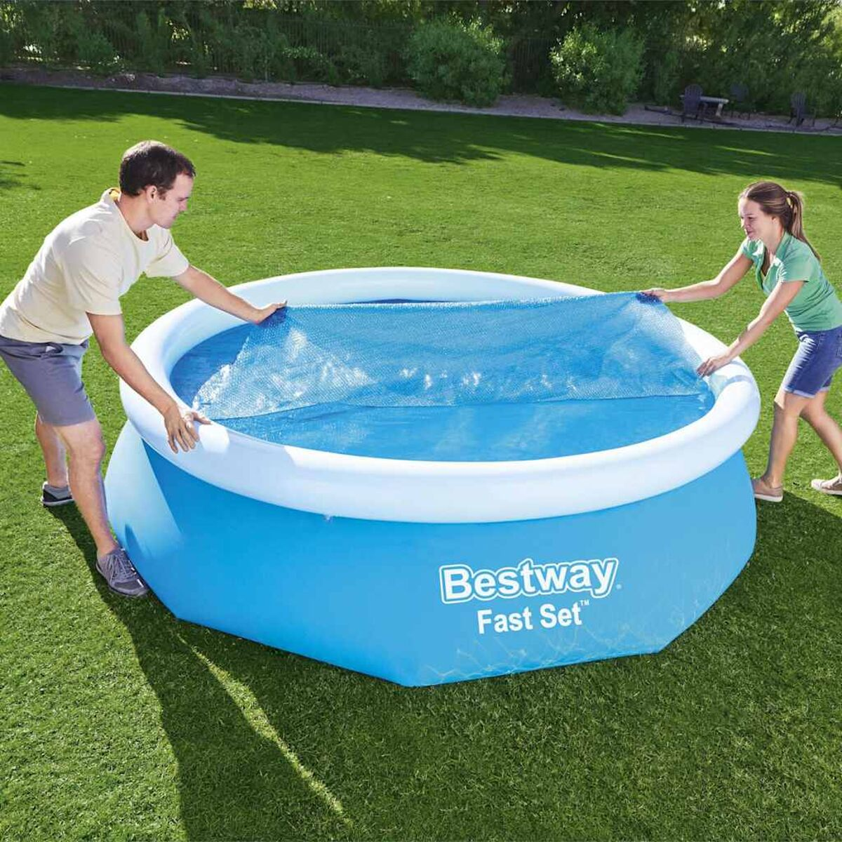 Zwei Personen bauen einen blauen oberirdischen Pool auf. Grünes Gras im Hintergrund.