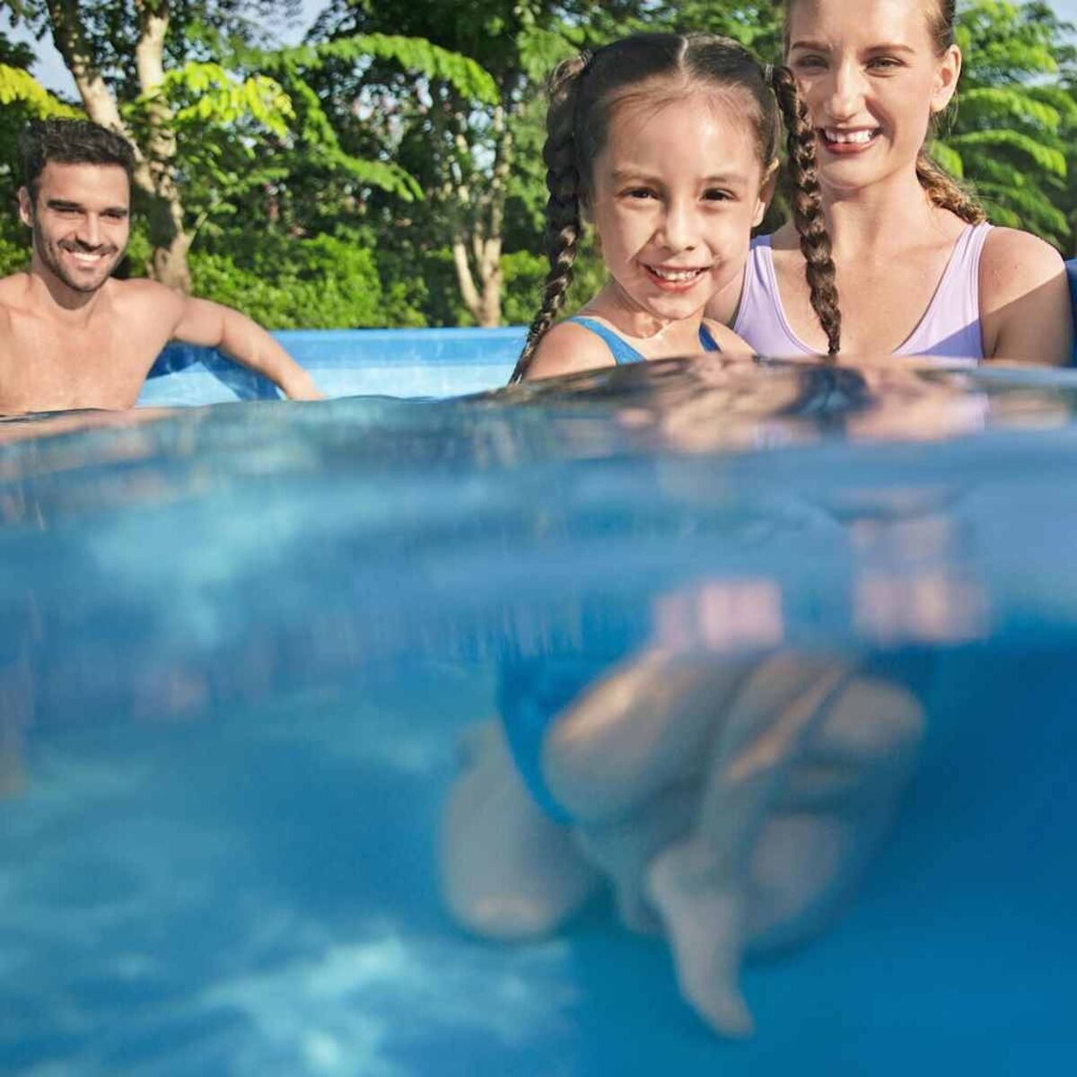 Ein Mann und zwei Mädchen in einem Schwimmbad. Das Wasser ist transparent. Der Hintergrund ist verschwommen.