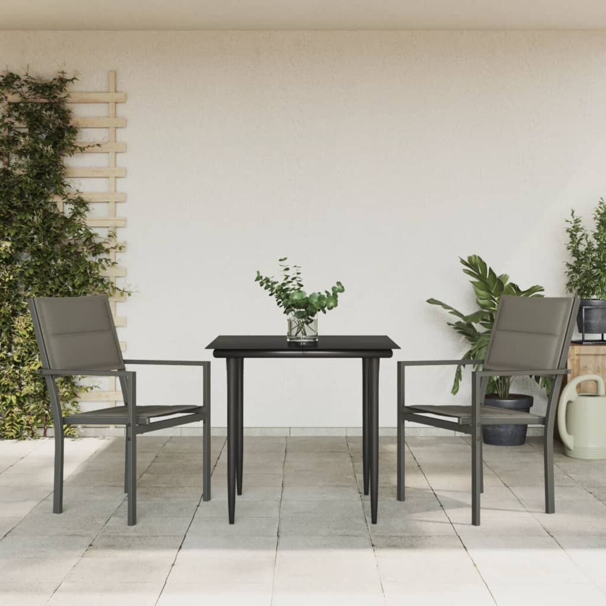 Ein Tisch und zwei Stühle auf einer Terrasse. Pflanzen sind im Hintergrund und an der Wand.