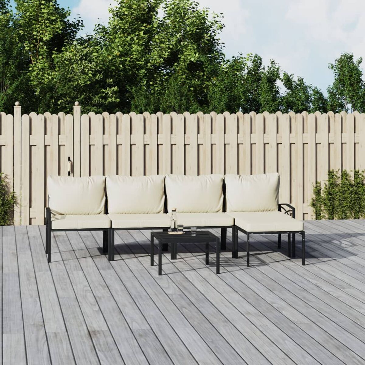 Outdoor-Terrassenset, schwarzer Metallrahmen, beige Kissen, auf Holzdeck, weißer Zaun, grüne Bäume.