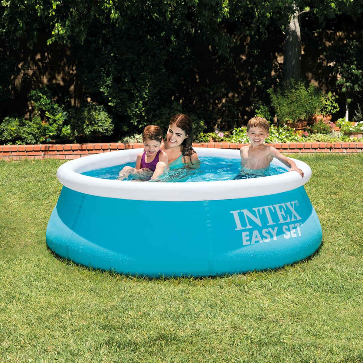 Drei Personen in einem blauen Intex-Pool auf Gras. Eine Frau und zwei Kinder genießen das Wasser. Hintergrund: Bäume und Ziegelmauer.