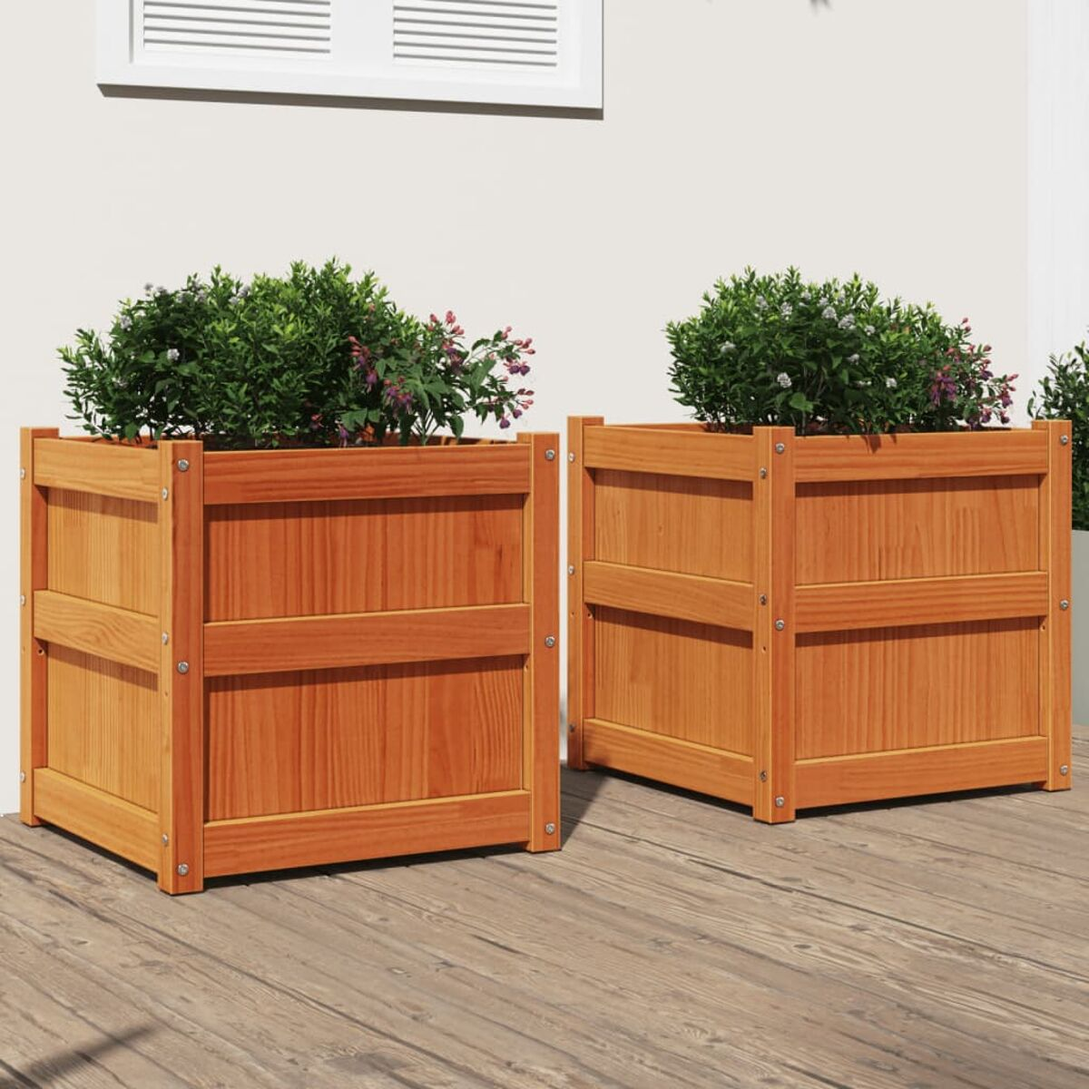 Zwei Holzpflanzkästen mit Pflanzen auf einem Holzdeck mit weißem Wandhintergrund.