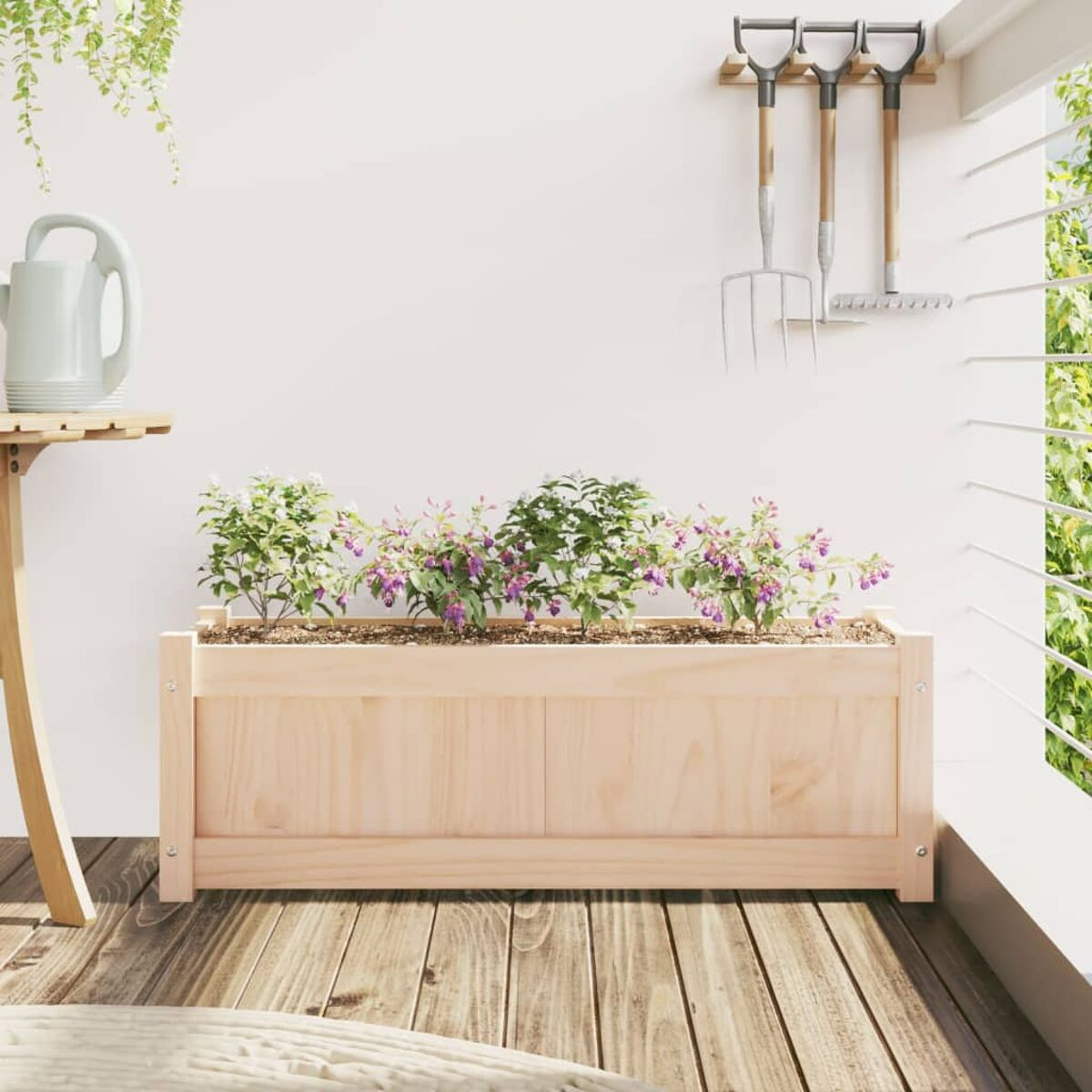 Holzpflanzkasten mit lila Blumen. Eine Gießkanne und Werkzeuge hängen dahinter an der Wand.