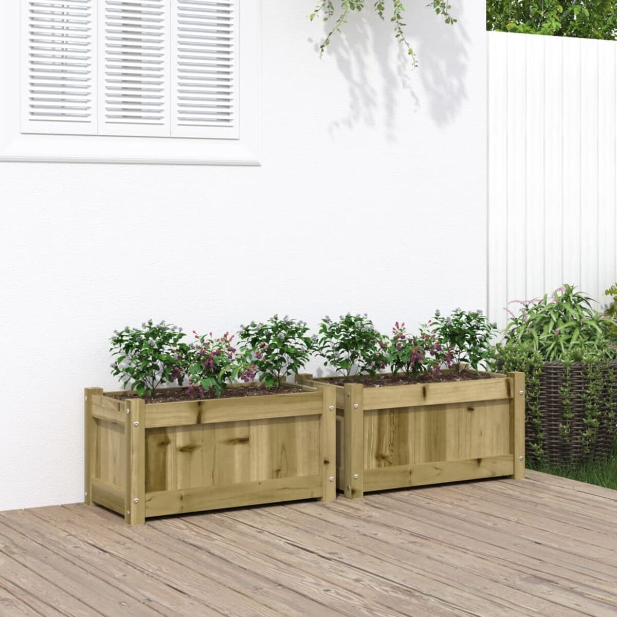 Zwei Holzpflanzgefäße mit Pflanzen auf einer Holzterrasse, vor einer weißen Wand und einem Fenster.