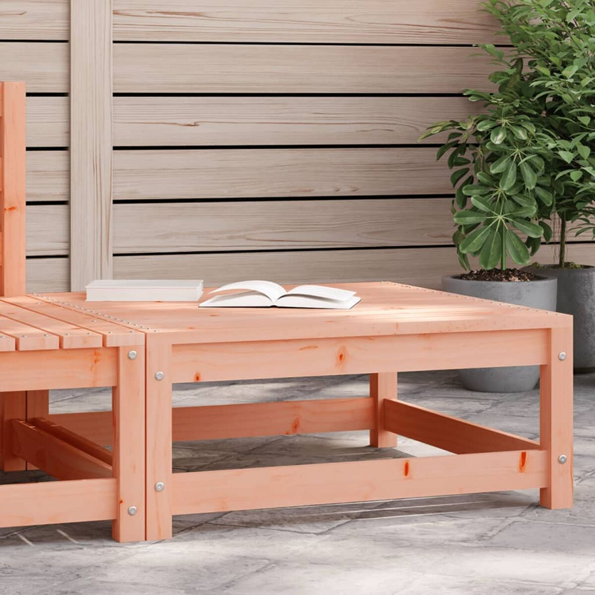 Ein Holztisch für draußen mit einem Buch und einer Pflanze. Der Tisch ist hellbraun mit Holzdeck.