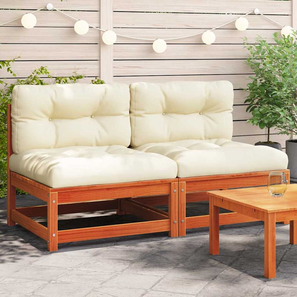 Outdoor-Sitzgruppe mit cremefarbenen Kissen und Holzrahmen, kleinem Tisch, Lichterkette und Wand.