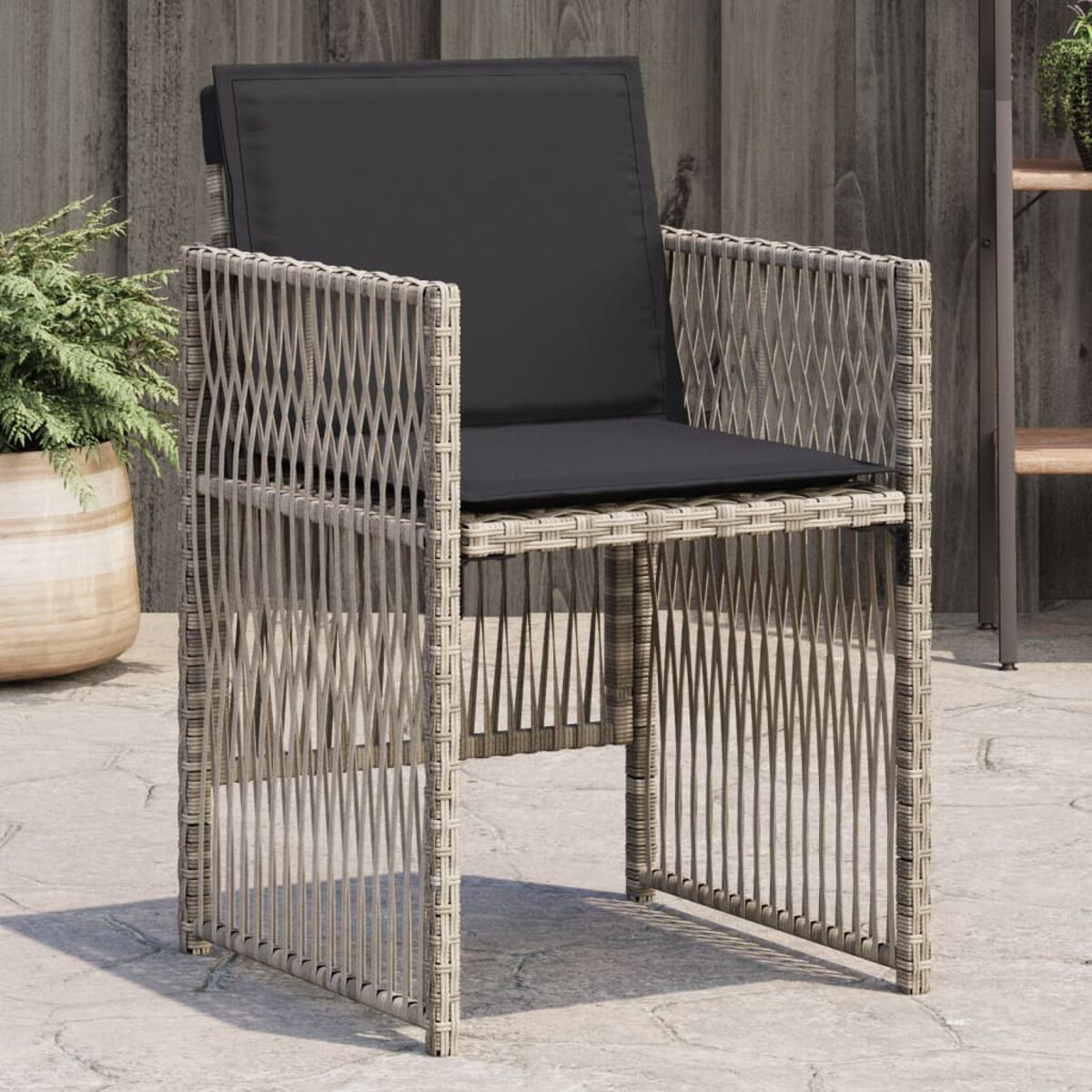 Una sedia in vimini con cuscino scuro su un patio, sullo sfondo naturale di una pianta.