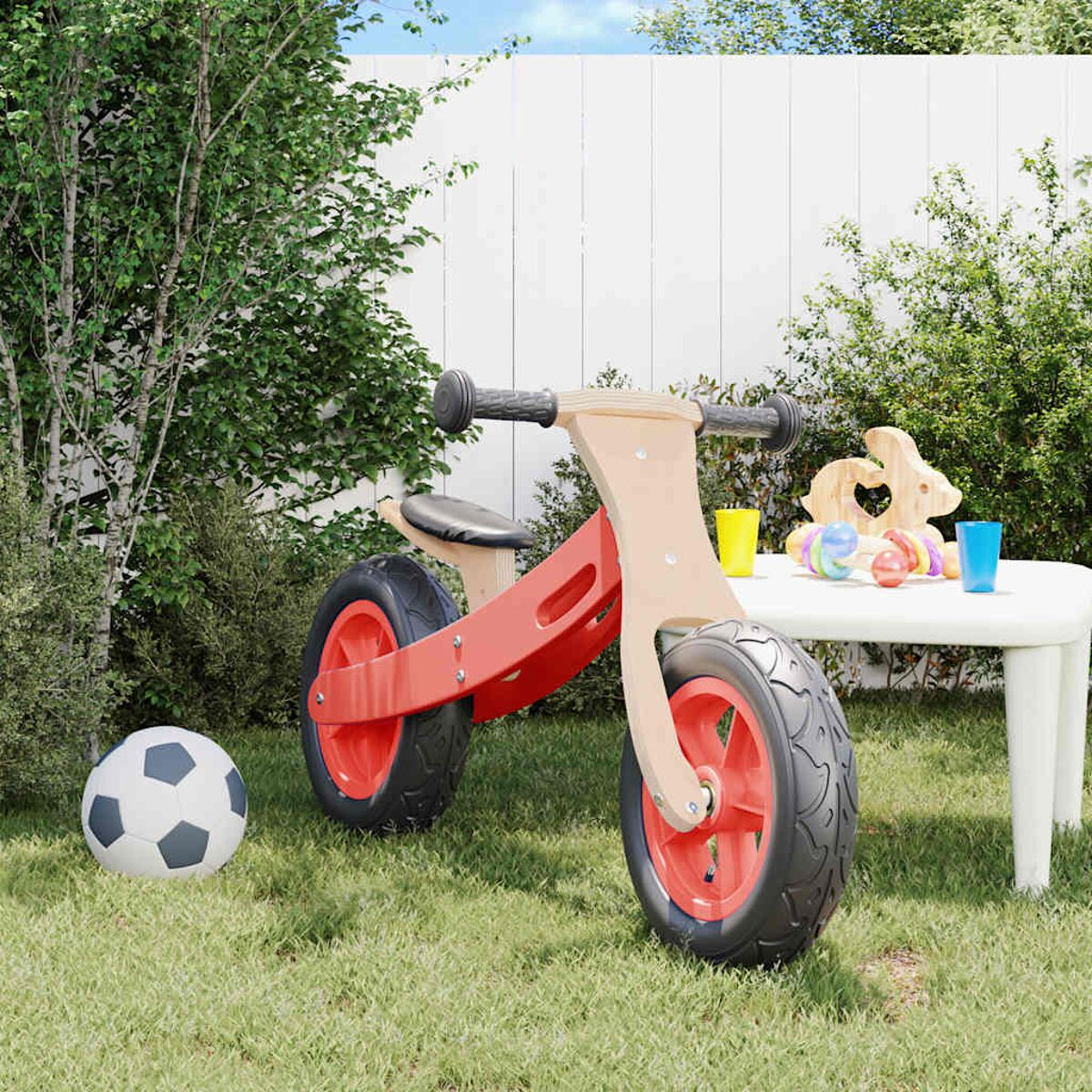 Ein rot-braunes Laufrad auf Gras, mit Spielzeug auf einem weißen Tisch.