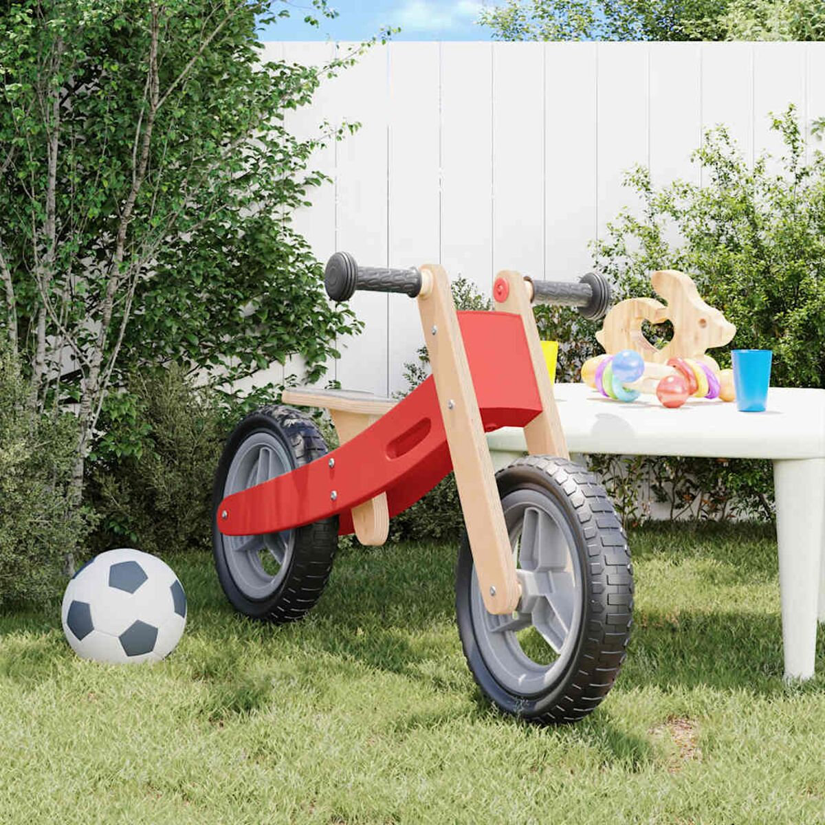 Rotes und Holz-Laufrad auf Gras, mit einem Fußball und Spielzeug auf einem weißen Tisch.