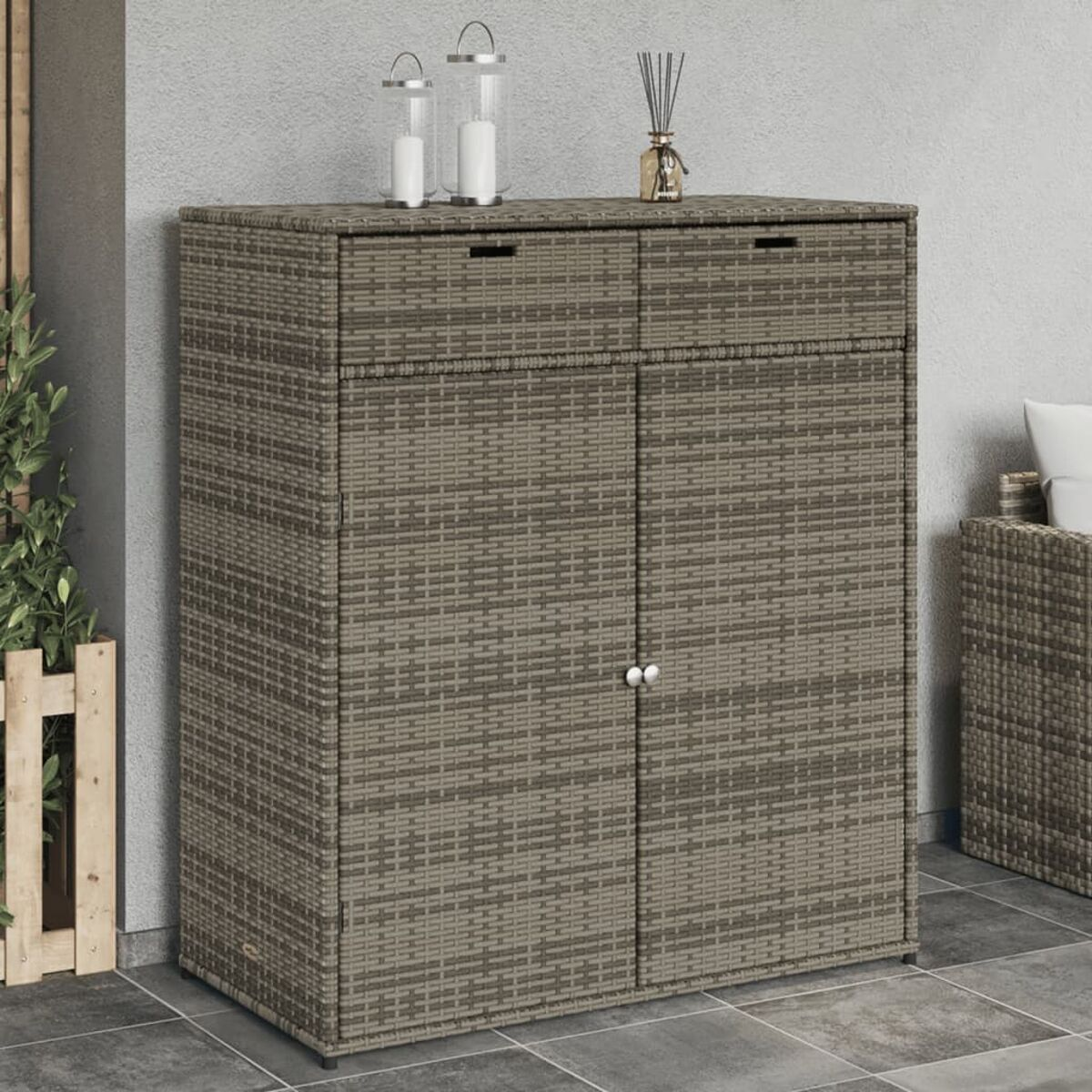 Ein Korbschrank mit zwei Türen und zwei Schubladen, platziert auf einer Terrasse mit zwei Laternen.