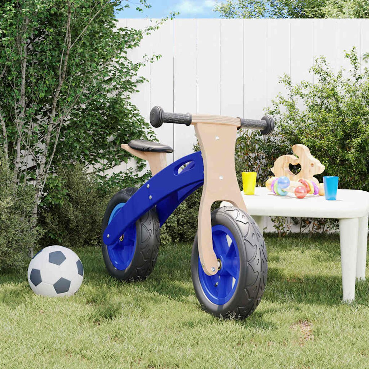 Blaues und hölzernes Laufrad auf Gras, neben einem weißen Tisch und Spielzeug.