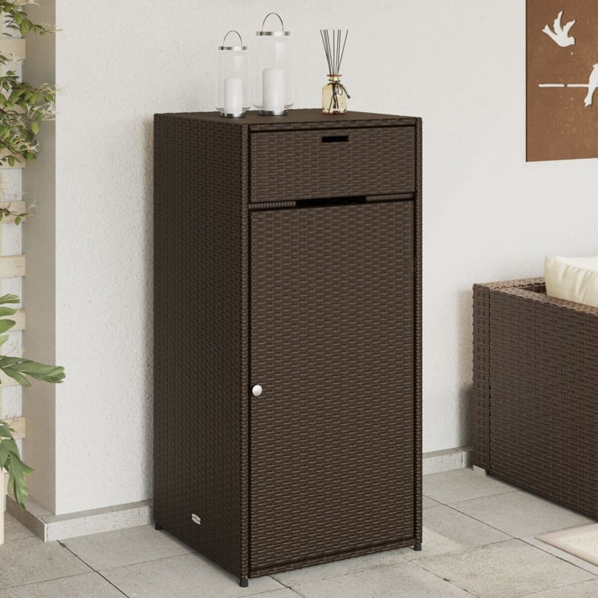 Ein brauner Outdoor-Aufbewahrungsschrank mit Schublade und Tür, mit Kerzen oben, vor einer weißen Wand.