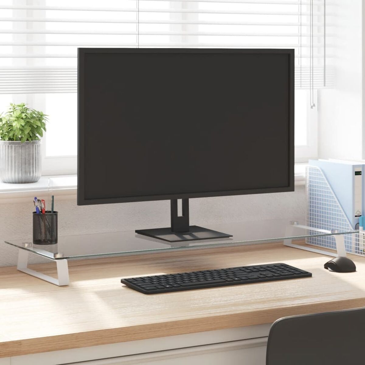 Schreibtisch mit Monitor auf Glasablage, Tastatur und Stifthalter. Fensterhintergrund.