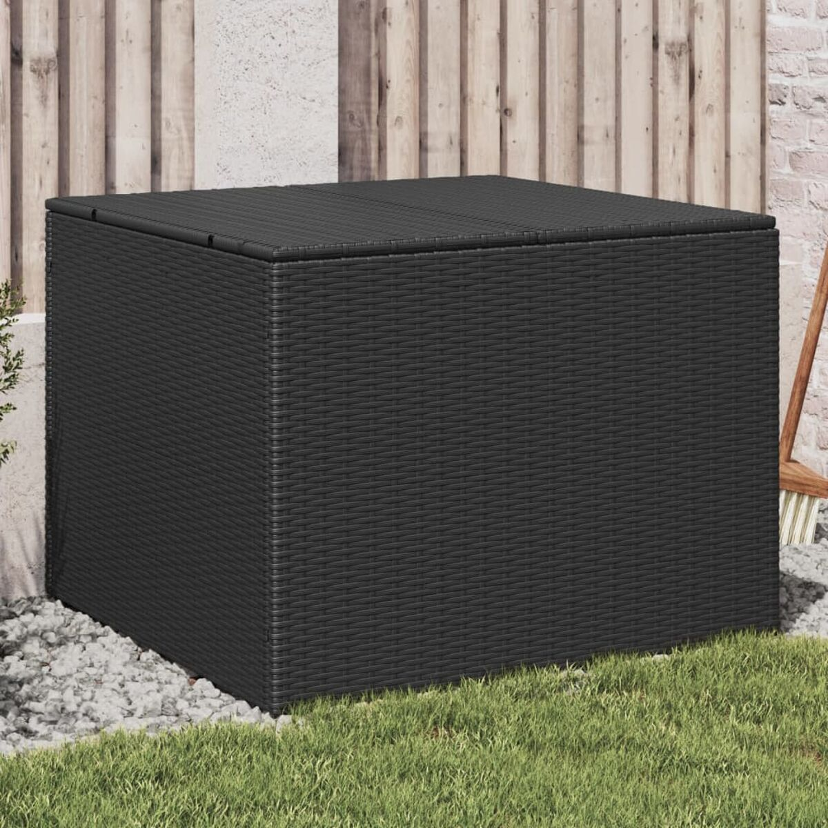 Schwarze Rattan-Würfel-Aufbewahrungsbox auf Kies, Gras und Holzzaun im Hintergrund.