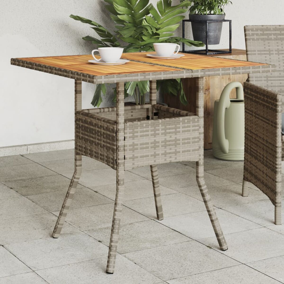 Quadratischer Outdoor-Tisch mit einem Korbboden und einer Holzplatte, mit Tassen und Tellern.