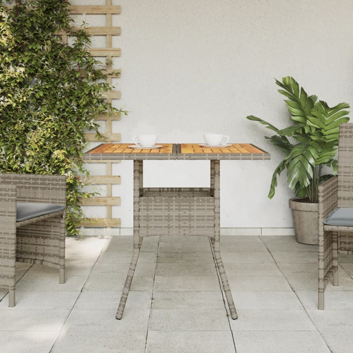 Ein kleiner Gartentisch mit zwei Tassen. Im Hintergrund links ein Holzgitter.