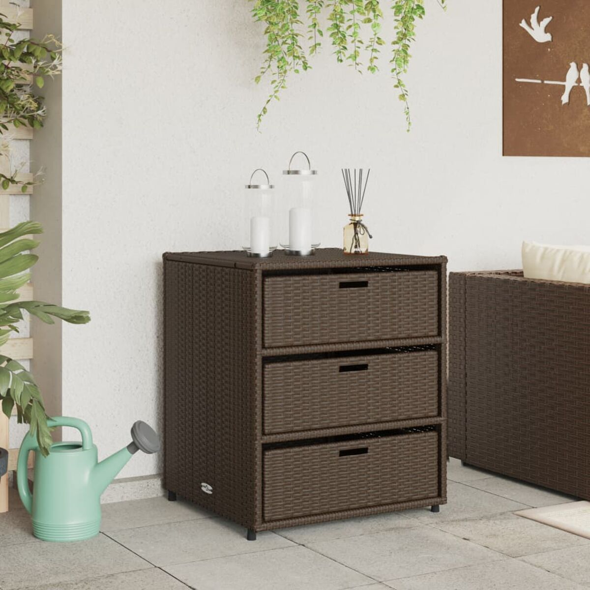 Brauner Korbschrank, drei Schubladen, Kerzen, eine Gießkanne auf einer Terrasse.
