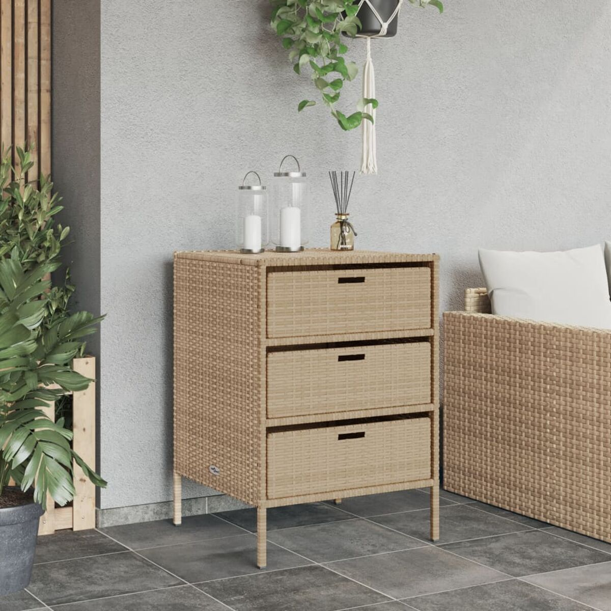 Wicker-Außenschrank mit drei Schubladen. Kerzen und eine Pflanze stehen oben. Grauer Fliesenboden.