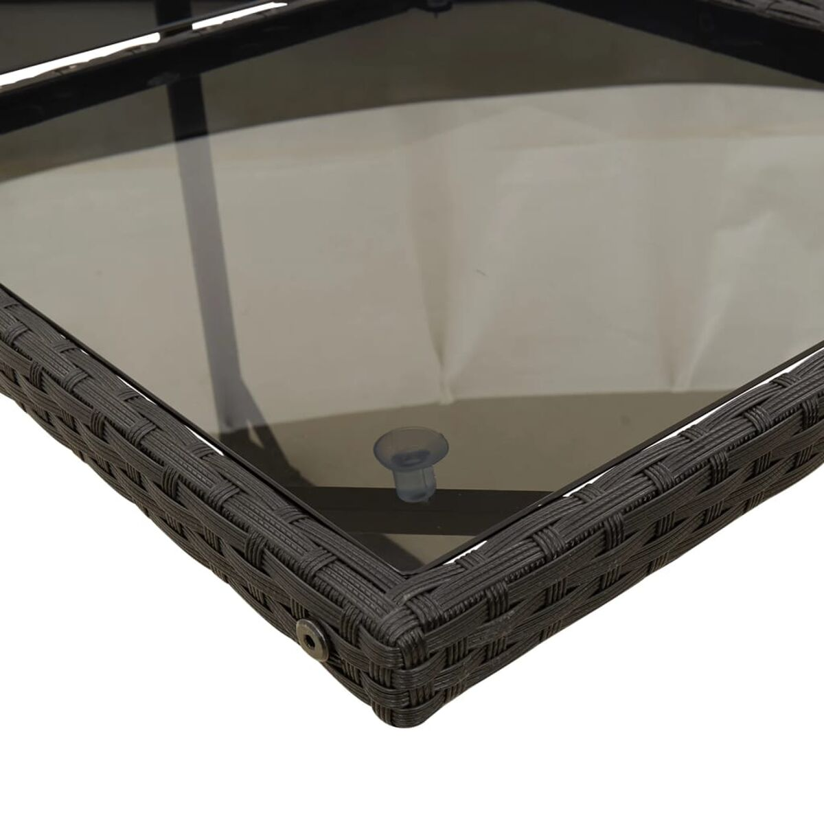 Primo piano di un angolo di tavolo intrecciato marrone scuro, con piano in vetro e ventosa trasparente.