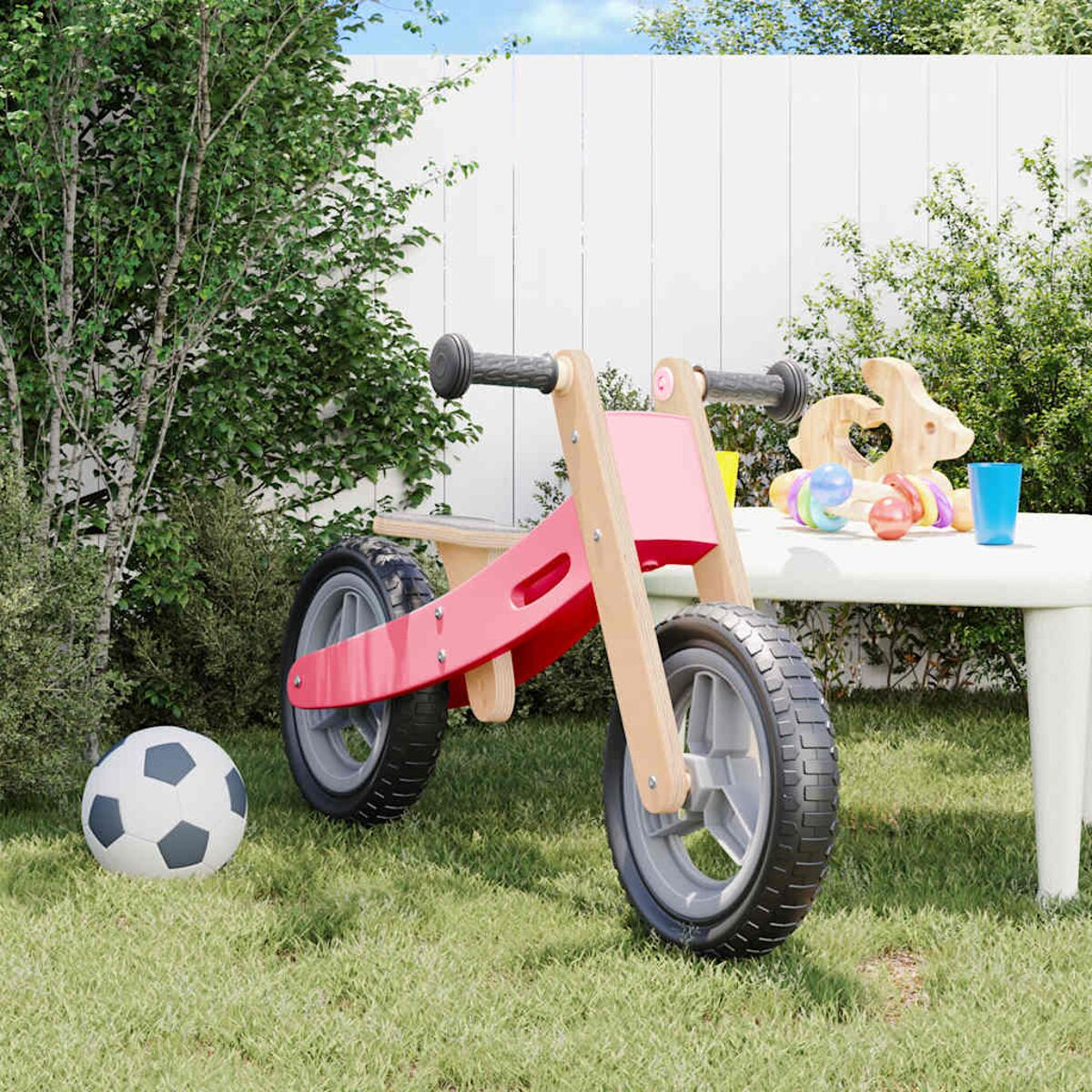 Rotes Laufrad mit Holzrahmen. Spielzeug und Ball auf weißem Tisch im Hintergrund.