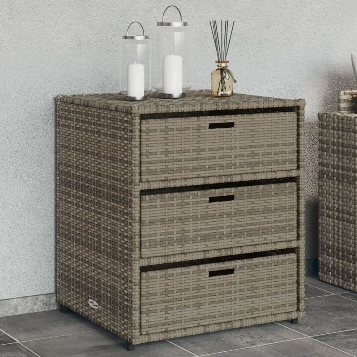 Ein grauer Korbgeflecht-Schrank mit drei Schubladen und Dekoration oben.