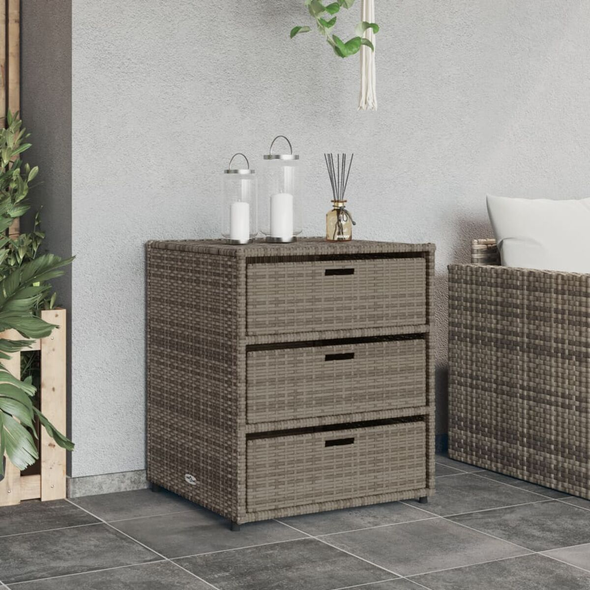 Rattan-Schrank mit drei Schubladen, Kerzen und Schilf-Diffusor. Vor grauer Wand.
