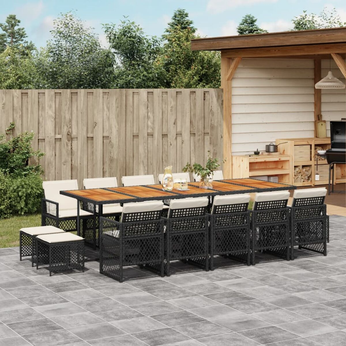 Garten-Essgruppe: großer Tisch, Stühle und Hocker auf einer Terrasse. Holzzaun und Garten im Hintergrund.