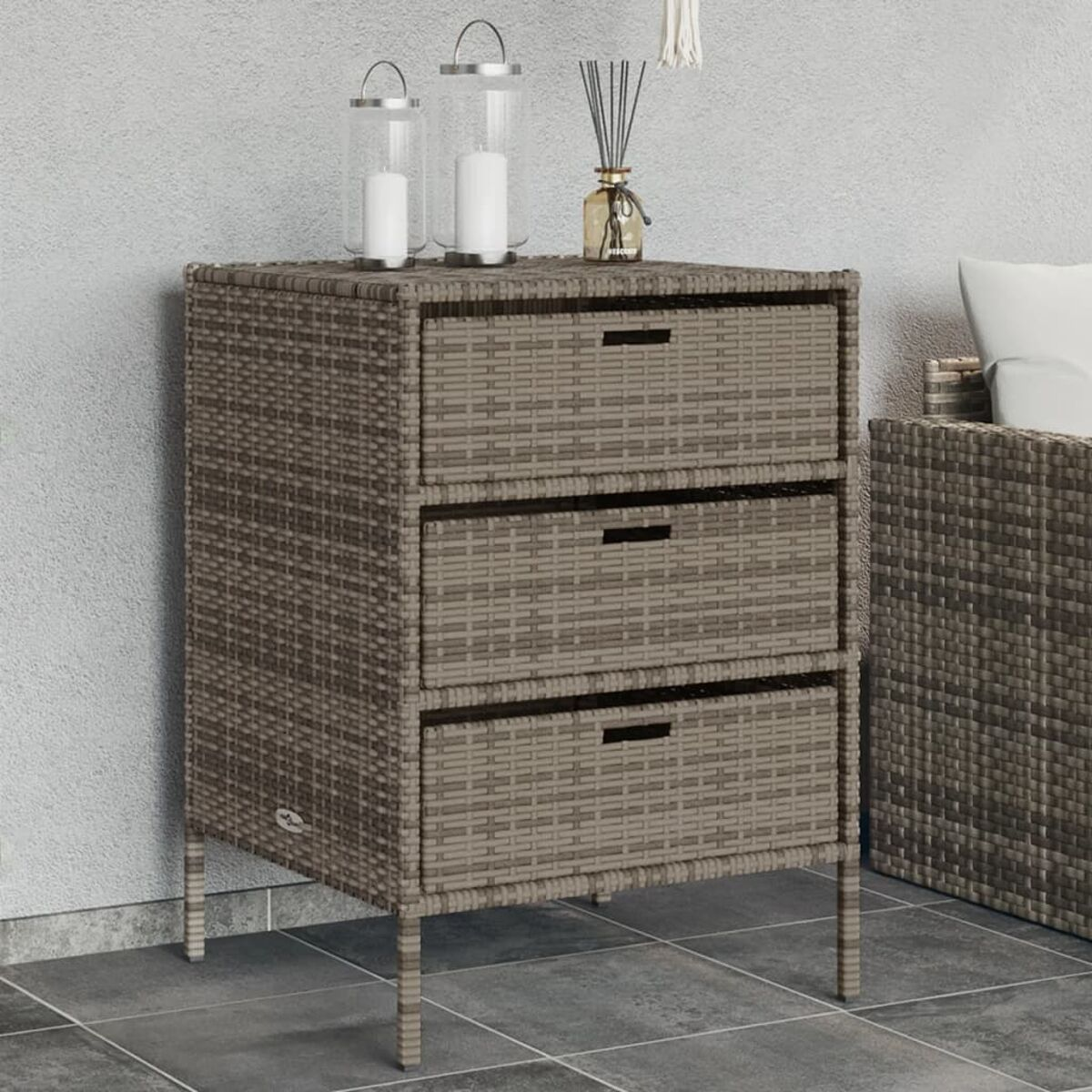 Korb-Schrank mit drei Schubladen. Zwei Kerzen und Vase mit Stöcken oben.
